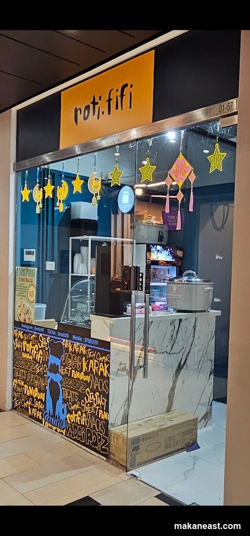 The storefront of a small eatery with the name "roti.fifi" displayed prominently above the entrance. The facade features large glass windows and doors, decorated with hanging star and moon ornaments. The lower part of the storefront is covered in a chalkboard-style design with various food items and social media handles listed. Inside, a counter area is visible with some equipment and display shelves.