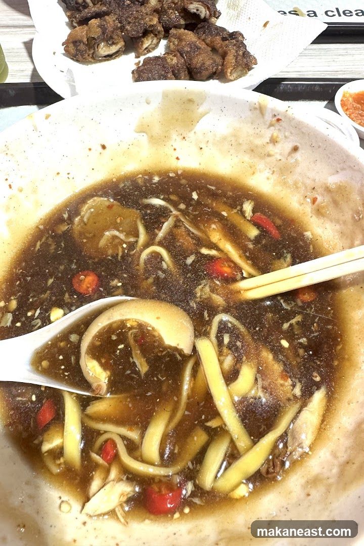 Close-up of a bowl of noodles with broth and a side of fried food