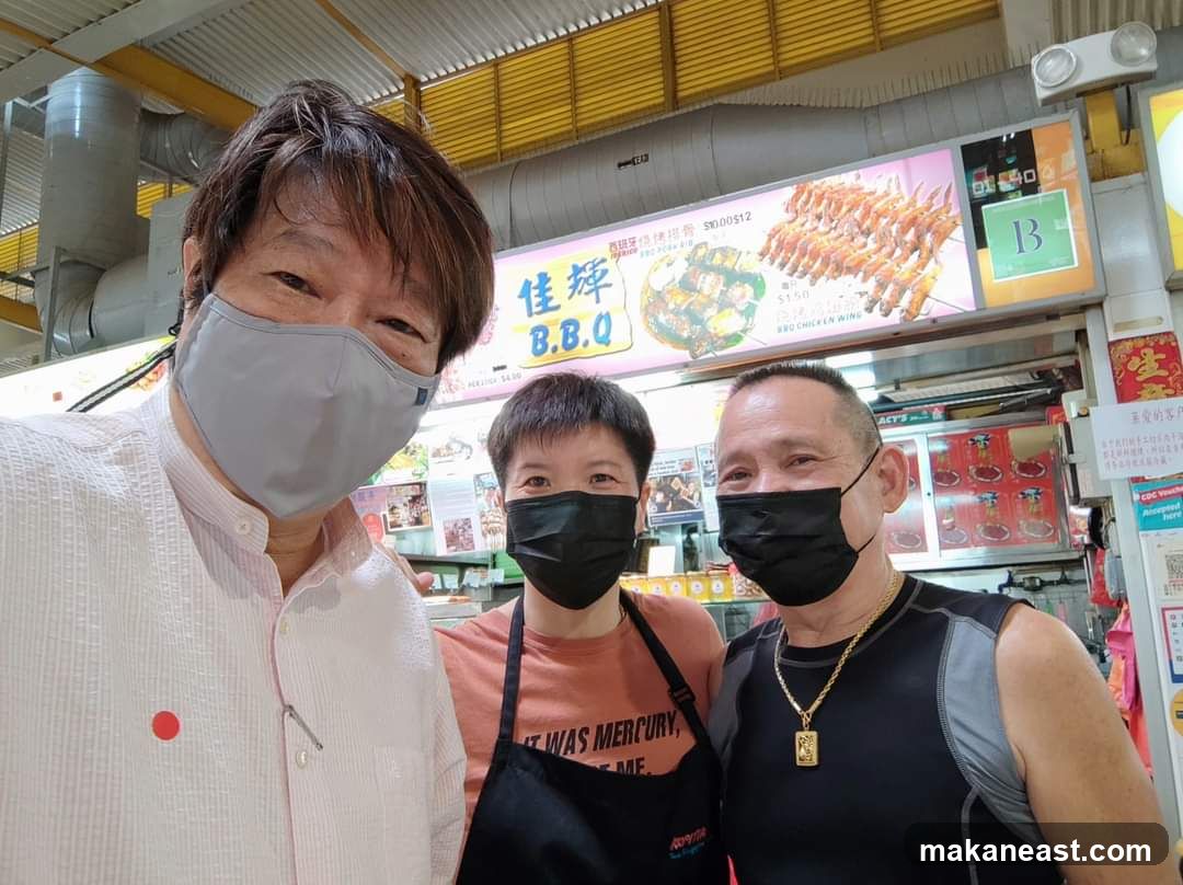 Three people posing for a selfie in front of a food stall