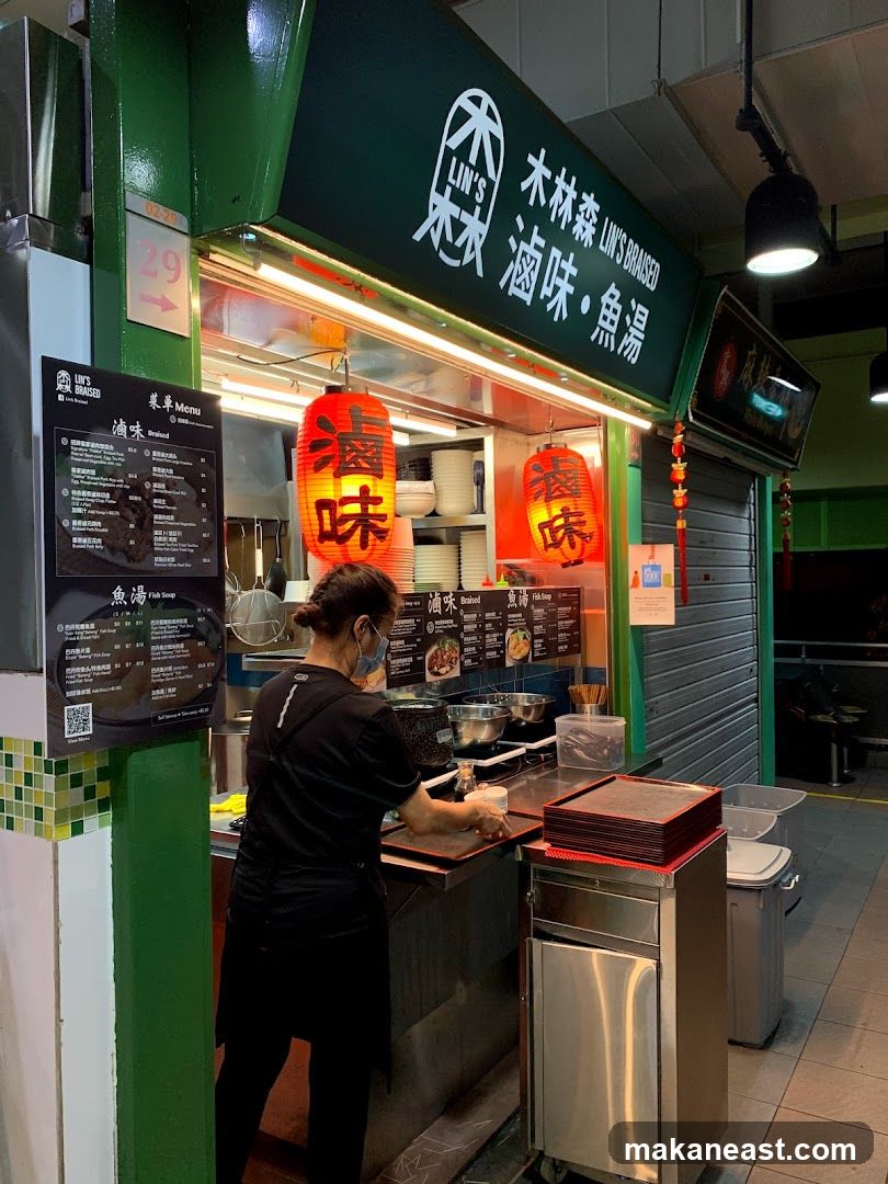 A food stall with a green facade and a sign that reads "LIN'S BRAISED" in English and Chinese. Two red lanterns with Chinese characters hang in front of the stall. A person wearing a black shirt and mask is working behind the counter. A menu board is visible on the left side of the stall.
