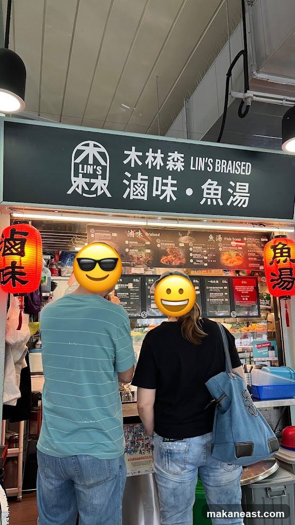 A food stall with a large sign displaying "LIN'S BRAISED" in English and Chinese characters. Below the main sign, there are menu boards with pictures and prices of various dishes. Two people are standing in front of the stall, looking at the menu. Red lanterns with Chinese characters hang on either side of the stall.