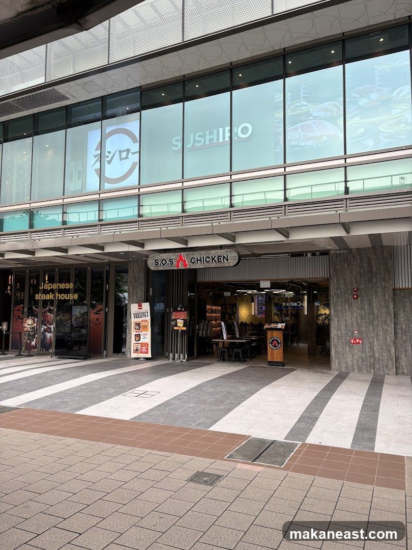 The exterior of a building with multiple storefronts. The storefronts visible are for "S.O.S CHICKEN" and a "Japanese steak house". Above these, on the second floor, is a large window with the "SUSHIRO" logo.