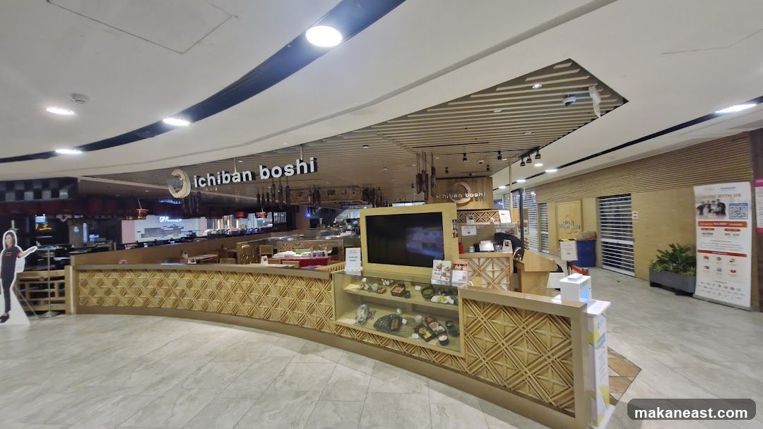 The exterior of the Ichiban Boshi restaurant, a Japanese eatery, is visible. The restaurant features a prominent sign with its name and logo. The interior seating area and a display counter with food models are also visible. A promotional banner is placed to the right of the entrance.
