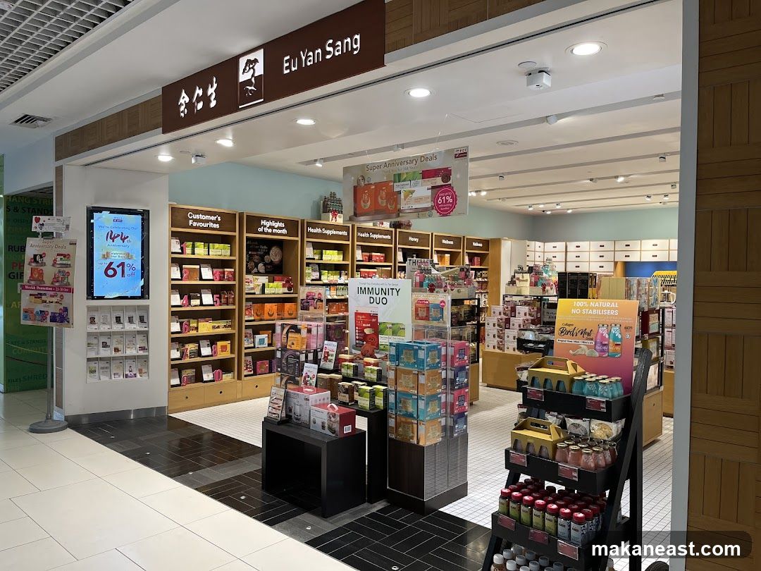 The exterior of a Eu Yan Sang store, featuring a prominent sign with the store name and logo. Inside, shelves are stocked with various health supplements and products. A digital display shows "Super Anniversary Deals" with a 61% discount. Promotional posters and product displays are visible throughout the store.