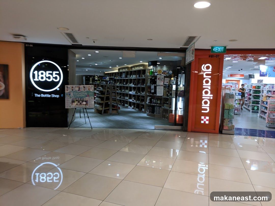 The exterior of two adjacent shops. The shop on the left is '1855 The Bottle Shop' with a large circular logo and the text 'The Bottle Shop' below it. A promotional poster is displayed in front of this shop. The shop on the right is 'Guardian', a health and beauty store, with its prominent orange signage. An 'EXIT' sign is visible above the Guardian entrance. The floor reflects the logos of both shops.