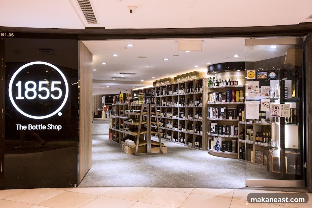 The exterior of a bottle shop with a large black glass facade featuring the logo "1855 The Bottle Shop". The interior of the shop is visible, displaying shelves stocked with numerous bottles of wine and spirits.