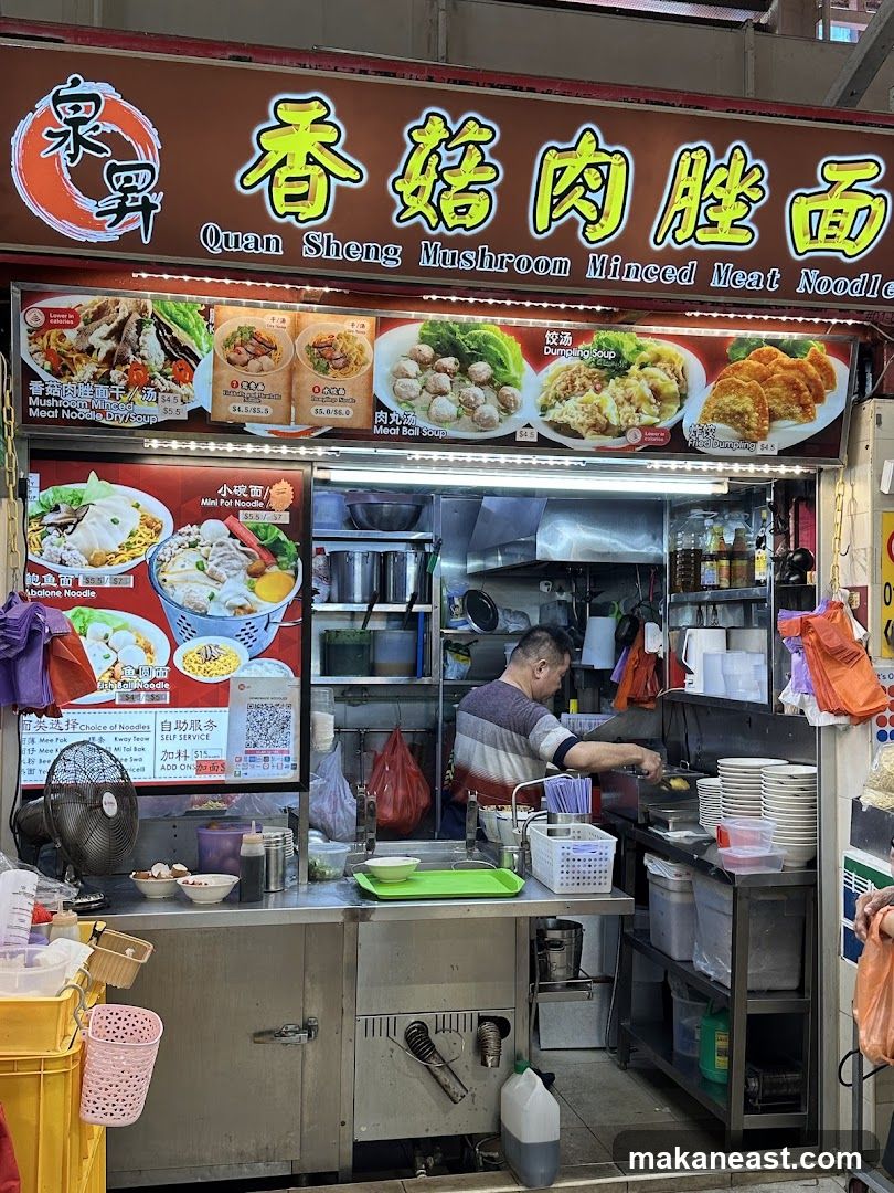 A food stall with a large sign displaying the business name and various noodle dishes. A chef is visible working behind the counter.