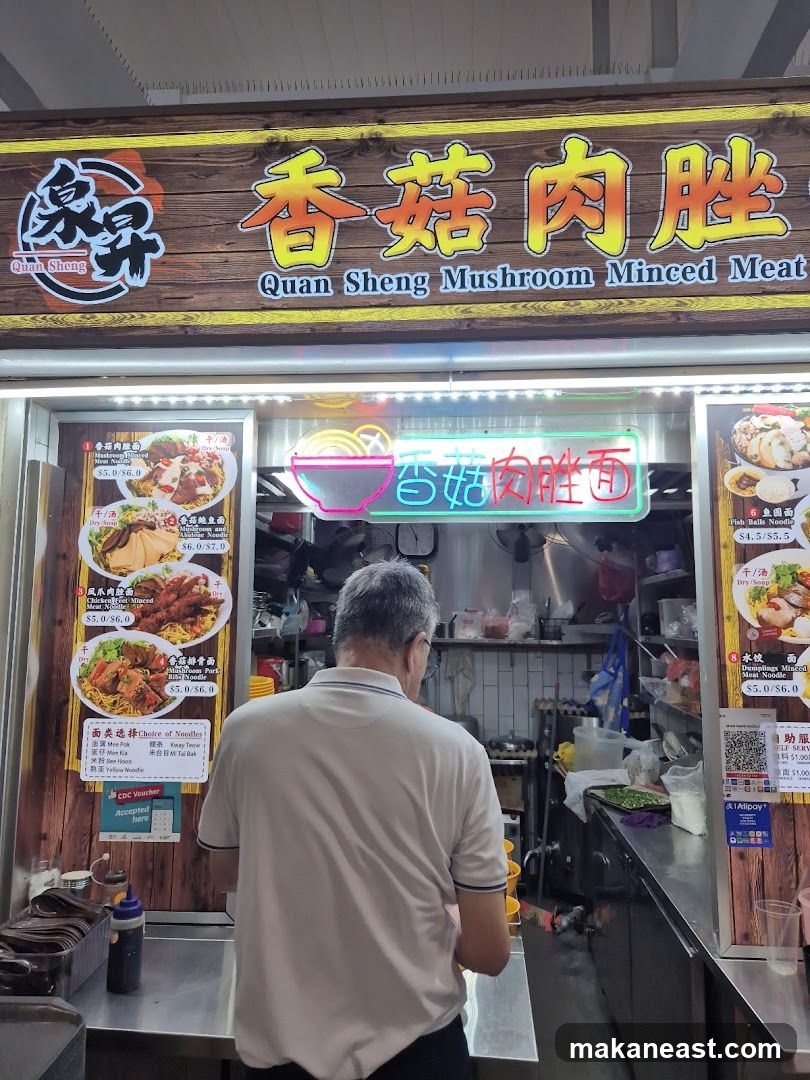 A man stands in front of a food stall with a large wooden sign above that reads "Quan Sheng Mushroom Minced Meat" in English and Chinese. Below the sign, a menu displays various noodle dishes with prices. The stall appears to be open with food preparation visible in the background.
