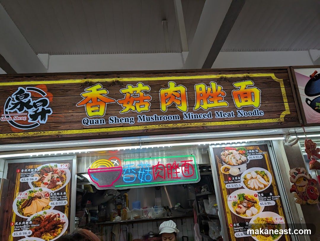 A close-up shot of a food stall's signage and menu displays. The main sign features the name "Quan Sheng Mushroom Minced Meat Noodle" in both Chinese characters and English, set against a wooden background. Below the main sign, illuminated menu boards showcase various noodle dishes with images and prices. A neon sign with Chinese characters and a bowl of noodles is also visible.