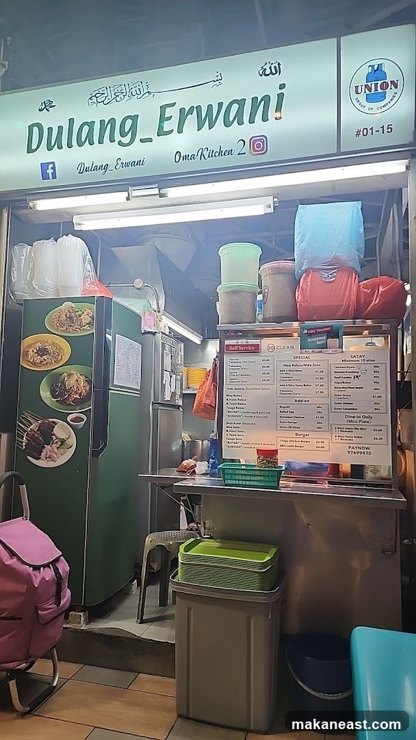 A food stall with a sign that reads "Dulung_Erwani" and social media handles. There are pictures of food on the side of a refrigerator and a menu board displaying various dishes and prices. The stall has a "Self Service" sign and a "SG CLEAN" sticker.