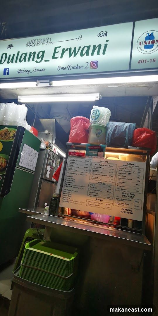 A storefront with a sign that reads "Dulung_Erwani" and "Oma Kitchen 2". Below the sign, there is a menu board with various food items and prices.