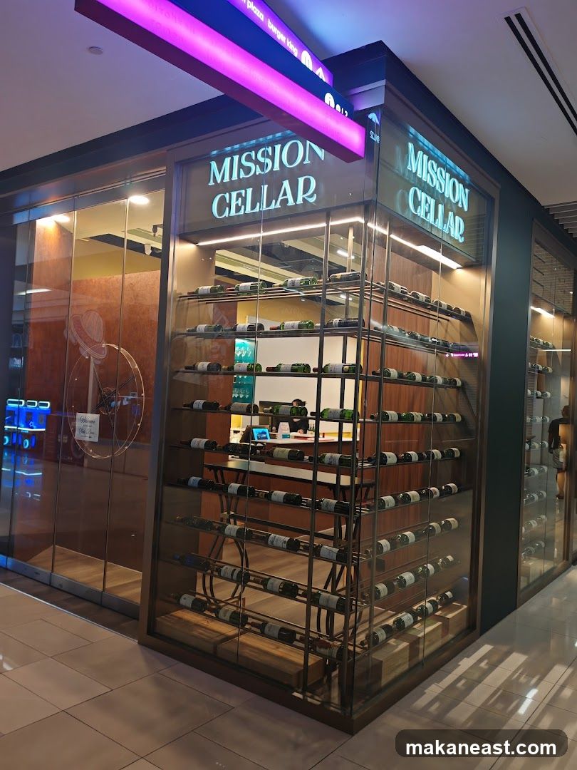 A corner view of the Mission Cellar shop front. The store has a glass facade displaying rows of wine bottles on shelves. The store name "MISSION CELLAR" is visible in illuminated lettering above the entrance.