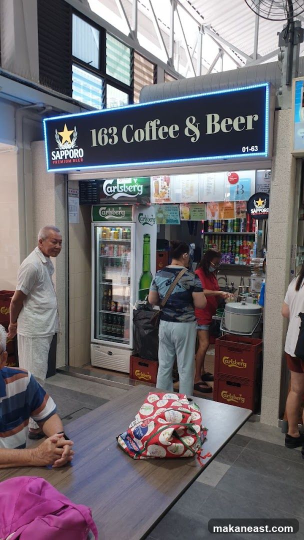 A storefront for 163 Coffee & Beer, with a prominent illuminated sign. A refrigerator stocked with beverages is visible, along with several people interacting with the staff. Tables and chairs are set up in front of the shop.