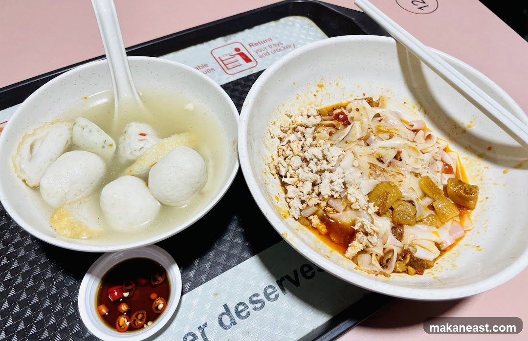 A close-up shot of two bowls of food on a tray. The bowl on the left contains fishball soup with several fishballs, fish cakes, and fried tofu. The bowl on the right contains flat noodles with minced meat and fried dough bits. A small dish of chili and soy sauce is also visible.