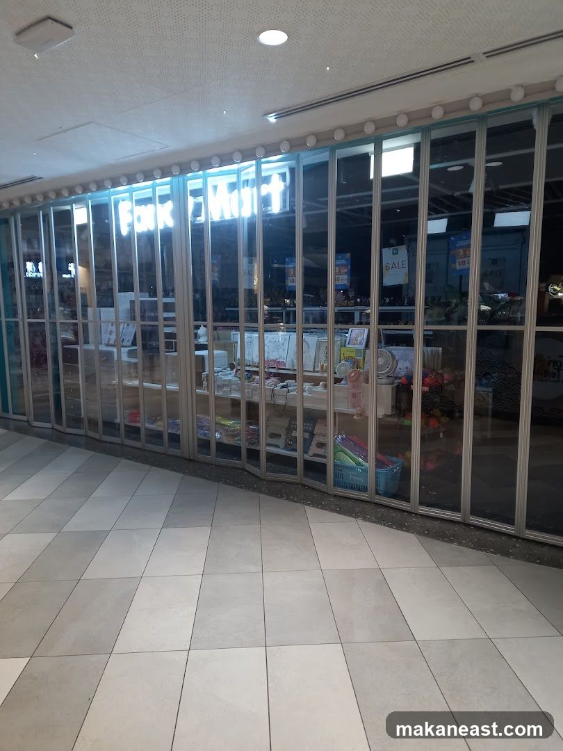 The storefront of a shop called Fank Mart, with its name illuminated in large white letters above a row of glass doors. The doors are folded open, revealing shelves stocked with various items, including crafts, stationery, and home decor. Signs indicating "SALE" are visible in the background.