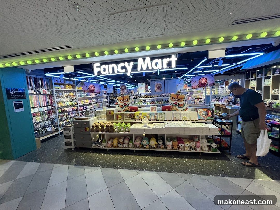 A man browses items in a brightly lit store called Fancy Mart. The store is filled with shelves stocked with various goods, including stuffed animals, stationery, and other novelty items. A large sign above the entrance reads "Fancy Mart."