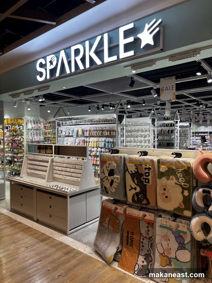 The exterior of a retail store named Sparkle, with its illuminated sign visible above the entrance. The store displays a variety of merchandise, including accessories, mats with cartoon designs, and travel pillows. Sale signs are also visible.