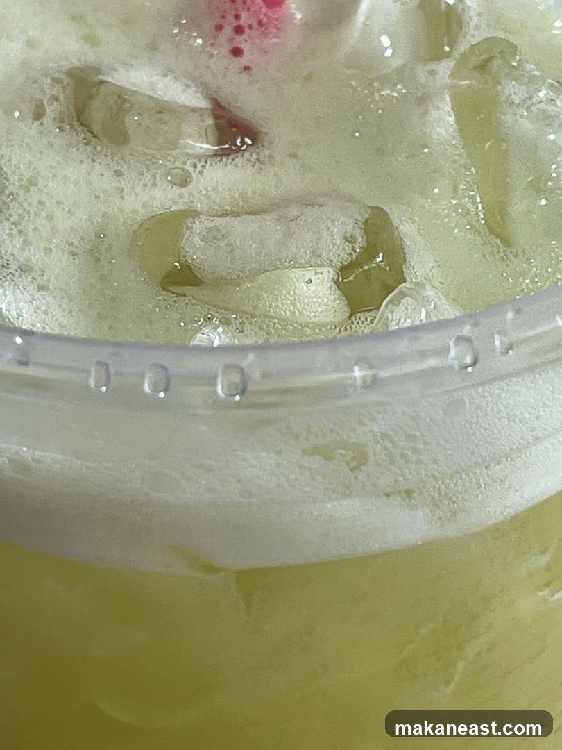 Close-up of a frothy green beverage with ice