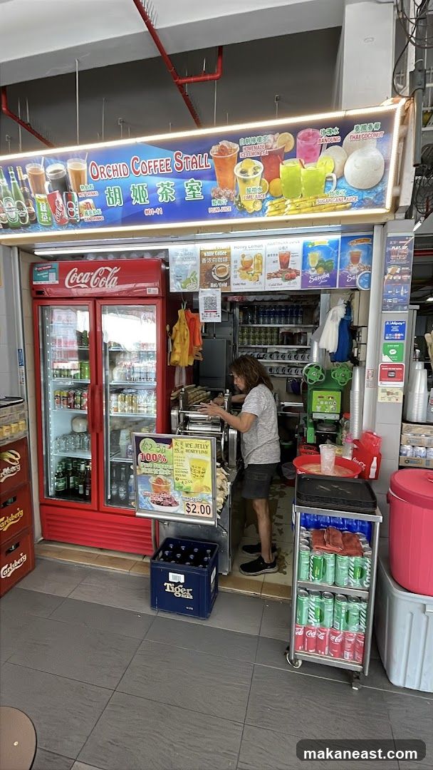 A street-level view of a coffee stall with a red Coca-Cola refrigerator on the left. The stall has a large illuminated sign above featuring various drinks and the name "ORCHID COFFEE STALL" in English and Chinese. A person is seen operating a sugarcane juicing machine. Various canned drinks and bottles are displayed in refrigerators and on shelves. A crate of Tiger beer is on the floor.