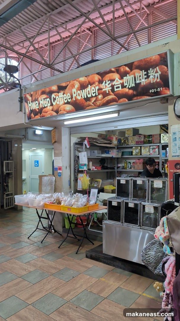 A storefront displaying bags of coffee powder and other goods. A sign above the entrance reads "Hwa Hup Coffee Powder" with Chinese characters and a unit number. Tables in front of the shop are laden with plastic bags of products. Inside, shelves are stocked with various items, and a person is visible behind a counter with large containers.