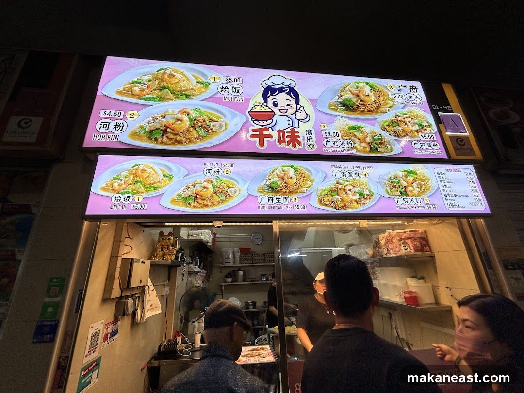 A brightly lit menu board displaying various noodle and rice dishes with images and prices.