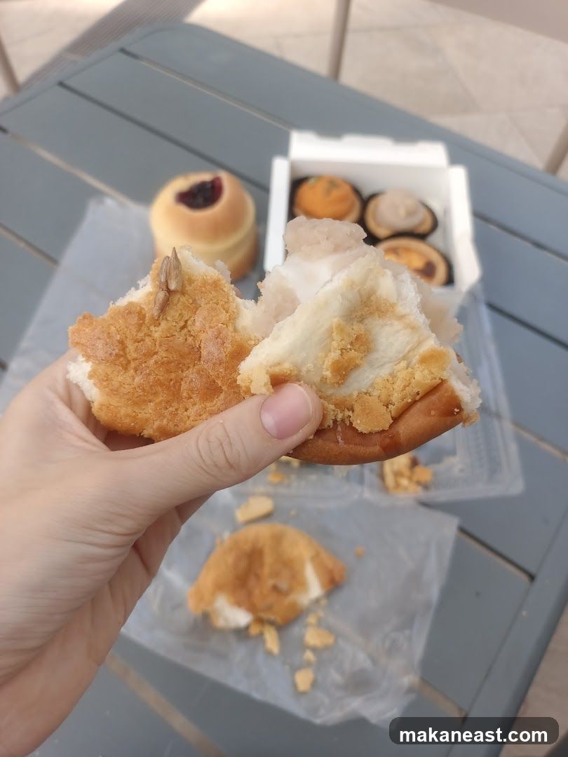 Hand holding a broken pastry with a box of pastries in the background