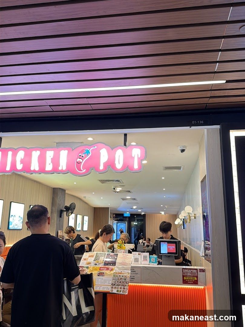 A brightly lit storefront with a pink neon sign that reads "CHICKEN POT" with a cartoon chili pepper. People are seen inside ordering and staff are behind the counter. There are menus displayed on stands.